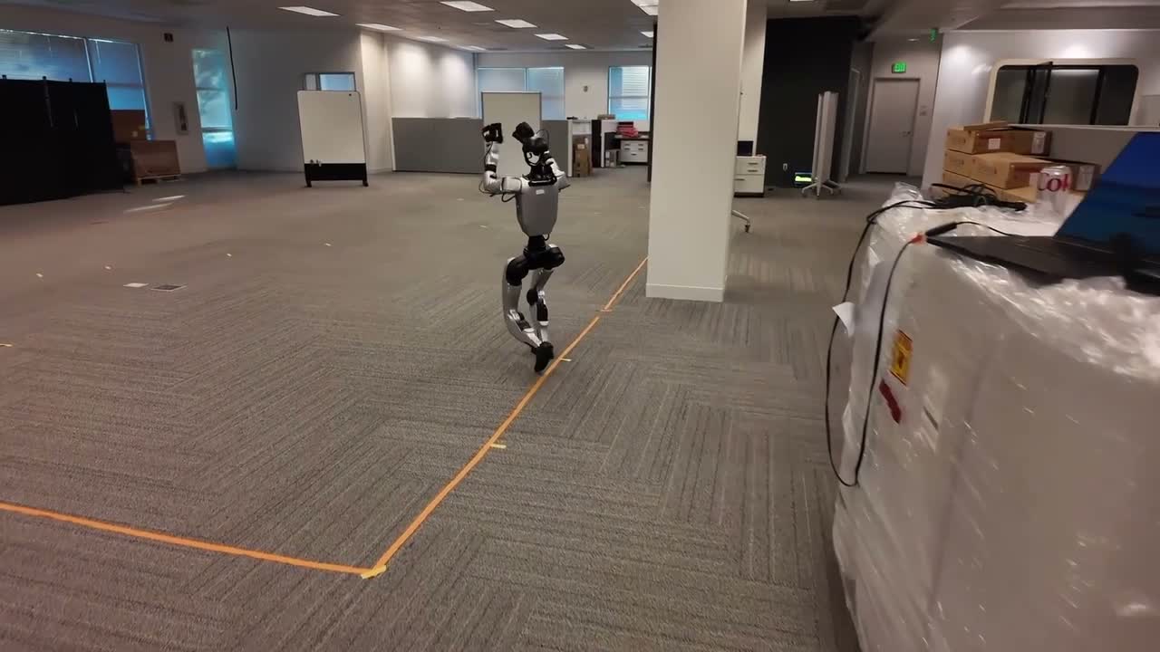A Unitree G1 humanoid robot moving across an indoor demonstration area