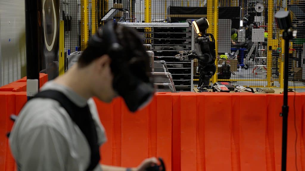 An operator wearing a VR headset trains Boston Dynamics’ Atlas robot inside an industrial facility.
